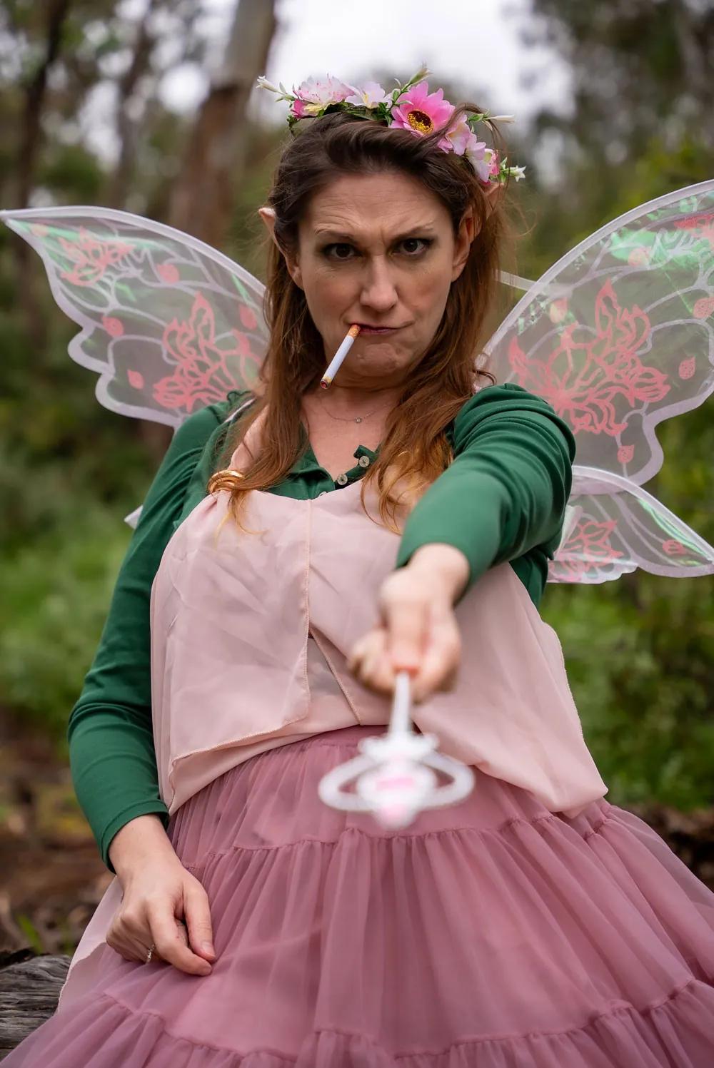 Thistle in a eucalyptus forest, glaring down the lens with a cigarette in her mouth and a toy wand pointed at the viewer.